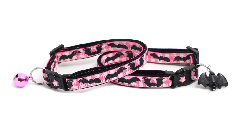 Puede incluir: Dos collares para gatos rosa y negro con un patr&oacute;n de murci&eacute;lago. Un collar tiene una campana rosa y el otro tiene un amuleto de murci&eacute;lago negro.
