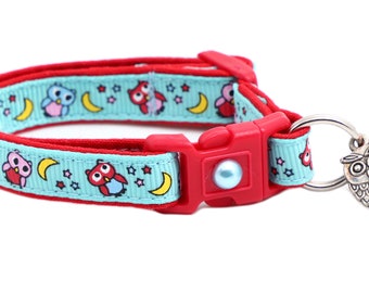 Puede incluir: Un collar para gatos rojo y azul claro con un diseño de búhos y lunas. El collar tiene una hebilla roja y un dije de búho plateado con una campana roja.