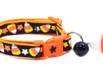 Puede incluir: Un collar de gato negro y naranja con un patrón de maíz dulce y una campana. El collar tiene una hebilla de seguridad y un amuleto en forma de estrella.