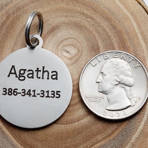 May include: A silver dog tag with the name Agatha and phone number 386-341-3135 engraved on it. The tag is next to a US quarter for size comparison.