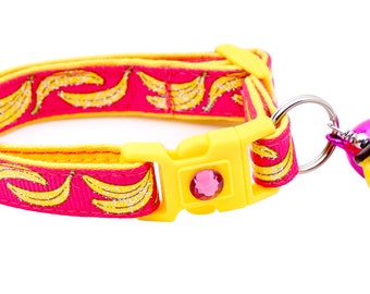 Puede incluir: Un collar para gato rosa y amarillo con estampado de plátano y un charm de campana amarilla. El collar tiene una hebilla de plástico y un cierre de seguridad.