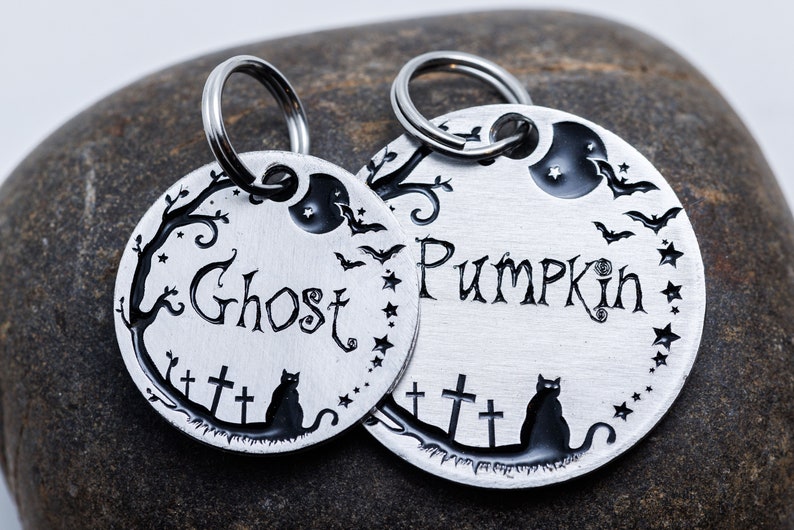 Pu&ograve; includere: Due medagliette per cani in argento con disegni incisi neri per Halloween. Una medaglietta dice "Ghost" e l'altra "Pumpkin". Entrambe le medagliette presentano un gatto nero, una luna crescente, pipistrelli e stelle.