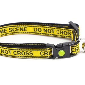 Op de afbeelding: Gele en zwarte hondenriem met de tekst "Crime Scene Do Not Cross" en een hartvormig label met de tekst "Here Comes Trouble".