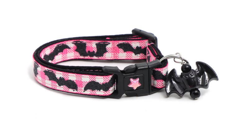 Puede incluir: Collar para gato de estampado rosa y negro con un dije de murci&eacute;lago negro. El collar tiene una hebilla negra y un dije en forma de estrella.