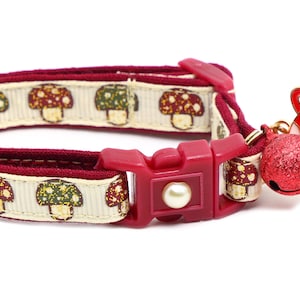 May include: A red and white mushroom-patterned cat collar with a red bell and a mushroom-shaped charm with a cat face.