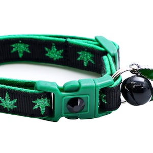 May include: A green and black cat collar with a green marijuana leaf charm and a bell. The collar is adjustable and has a safety release buckle.