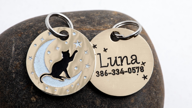 May include: Gold-toned pet ID tag with a black cat silhouette sitting on a crescent moon with stars. The other side of the tag has the name "Luna" and the phone number 386-334-0578.
