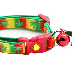 May include: A green, yellow, and red cat collar with a green leaf design and a red bell. The collar has a plastic buckle.