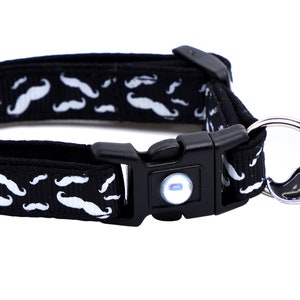 May include: Black cat collar with a white mustache pattern and a black bell with a silver mustache charm.