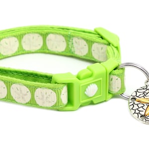 May include: A green cat collar with a white seashell pattern and a silver charm with a gold starfish. The charm is attached to a green bead.