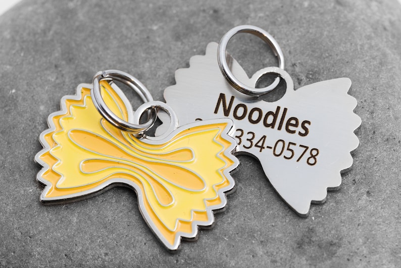 Pet tag shapes like farfalle (bowtie) pasta. The front is colored in yellow and orange tones to look like pasta. The back is silver and shows and example name and one phone number.