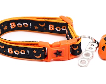 Puede incluir: Collar de gato negro y naranja con una campana en forma de calabaza y un dije plateado que dice "BOO!" El collar tiene un patrón repetido de estrellas, lunas y la palabra "BOO!"