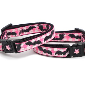 Puede incluir: Dos collares para gatos rosa y negro con un patr&oacute;n de murci&eacute;lago. Un collar tiene una campana rosa y el otro tiene un amuleto de murci&eacute;lago negro.