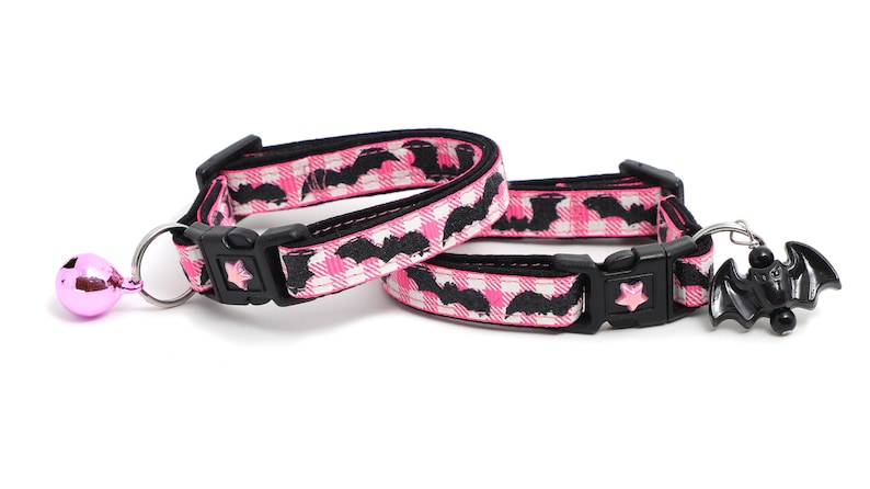 Puede incluir: Dos collares para gatos rosa y negro con un patr&oacute;n de murci&eacute;lago. Un collar tiene una campana rosa y el otro tiene un amuleto de murci&eacute;lago negro.