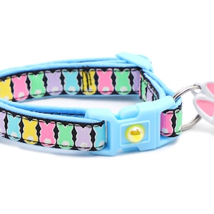 May include: A light blue cat collar with a colorful bunny pattern and a white bunny bell charm.