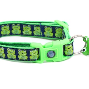 Puede incluir: Collar de gato verde con estampado de rana y una campana verde con forma de rana. El collar tiene una hebilla de plástico verde.