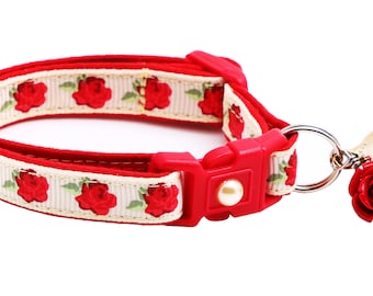 May include: A red and white cat collar with a floral pattern and a bell with a red rose charm.