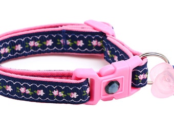 May include: A pink and navy blue cat collar with a floral pattern and a pink and blue bell charm.