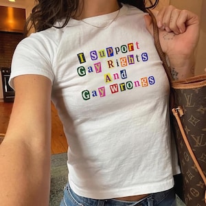 May include: A white short-sleeved t-shirt featuring the text I Support Gay Rights And Gay Wrongs printed in a colorful ransom note style with each letter enclosed in a small square box of varying colors including blue, green, yellow, and red.