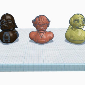 Könnte beinhalten: Drei Gummienten mit Charakter-Thema. Die Enten sind braun, orange und gelb und sind so gestaltet, dass sie Figuren aus einem beliebten Science-Fiction-Franchise ähneln. Die Enten werden auf einem blau-weißen Raster angezeigt.