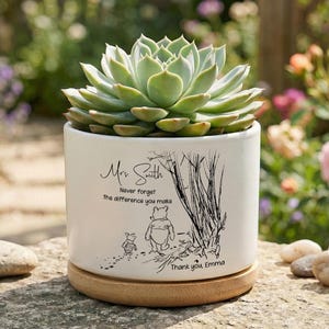 May include: A white ceramic planter with a succulent plant. The planter has a wooden base and features a black illustration of Winnie the Pooh and Piglet. Text on the planter reads "Mrs. Smith, Never forget the difference you make. Thank you, Emma."