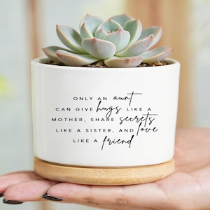 May include: White ceramic planter with a succulent plant. The planter has a wooden base and features the text: "Only an aunt can give hugs like a mother, share secrets like a sister, and love like a friend."
