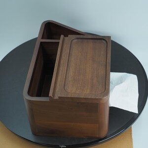 May include: A wooden tissue box with a rectangular shape and a sliding lid. The box is made of dark brown wood and has a smooth finish. A white tissue is partially visible.
