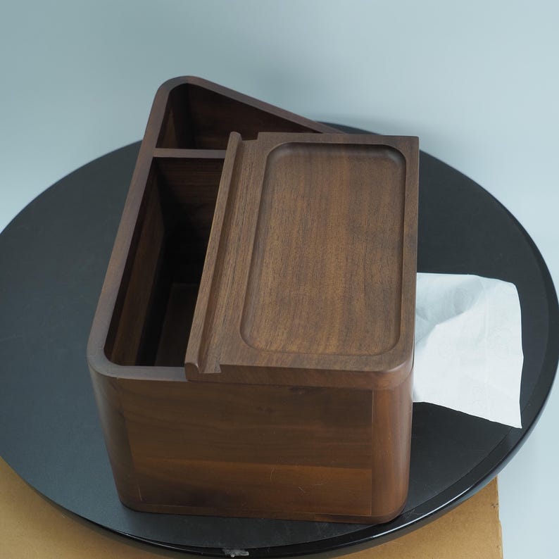 May include: A wooden tissue box with a rectangular shape and a sliding lid. The box is made of dark brown wood and has a smooth finish. A white tissue is partially visible.