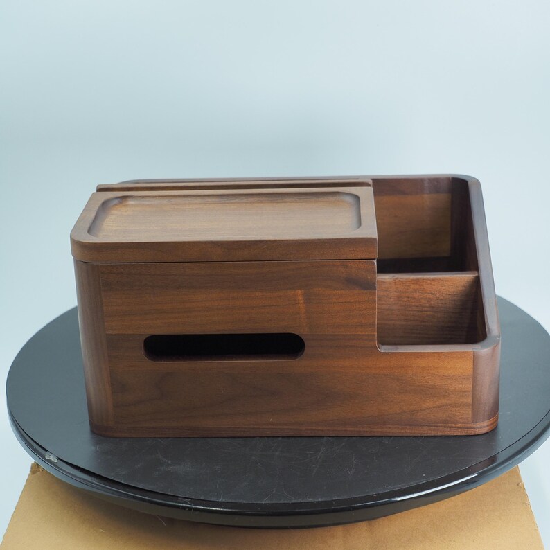 May include: A wooden desk organizer with a rich, dark brown finish. It features a sliding top, a compartment for tissues, and two open storage sections. The organizer is designed to hold various office supplies and keep a desk tidy.