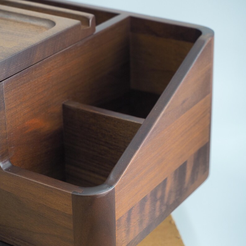 May include: A wooden desk organizer with multiple compartments and a dark brown finish. The organizer has a rectangular shape with rounded edges and a smooth surface. It is designed to hold various office supplies.