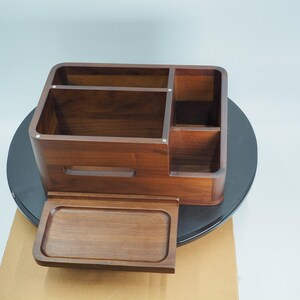 May include: A wooden desk organizer with multiple compartments and a pull-out tray. The organizer is made of dark brown wood and has a smooth finish. It features several sections for storing office supplies and other items.