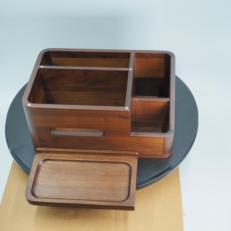 May include: A wooden desk organizer with multiple compartments and a pull-out tray. The organizer is made of dark brown wood and has a smooth finish. It features several sections for storing office supplies and other items.