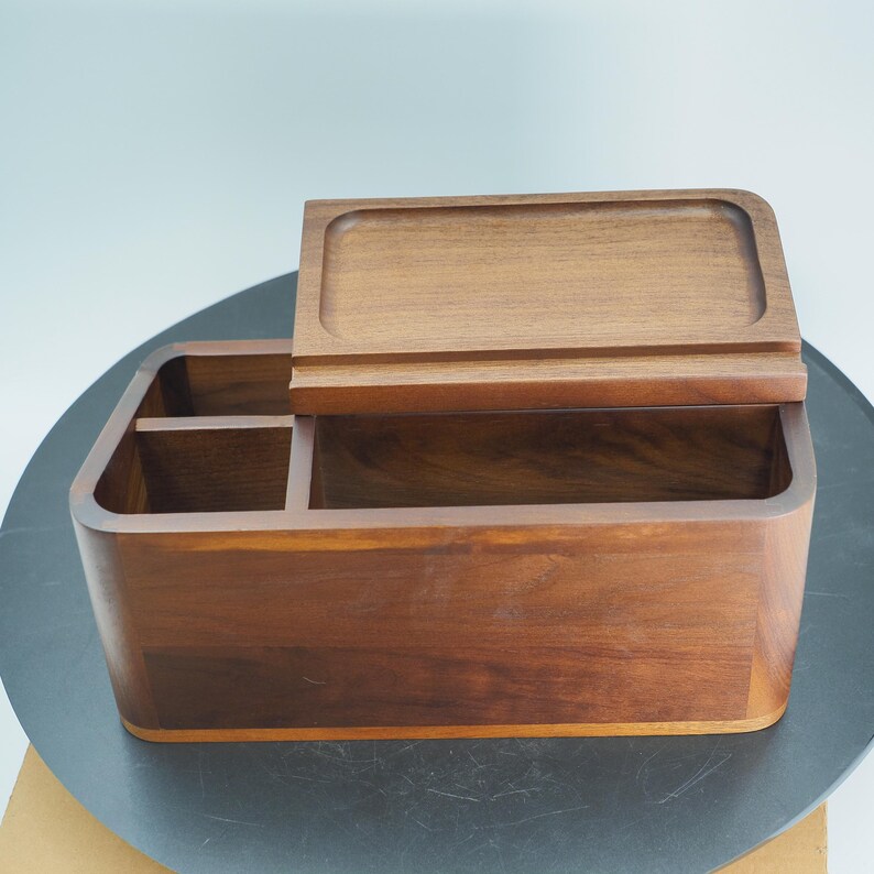 May include: A wooden desk organizer with a rectangular shape and a hinged lid. The organizer has multiple compartments and is made of a warm brown wood. The lid is partially open, revealing the interior.