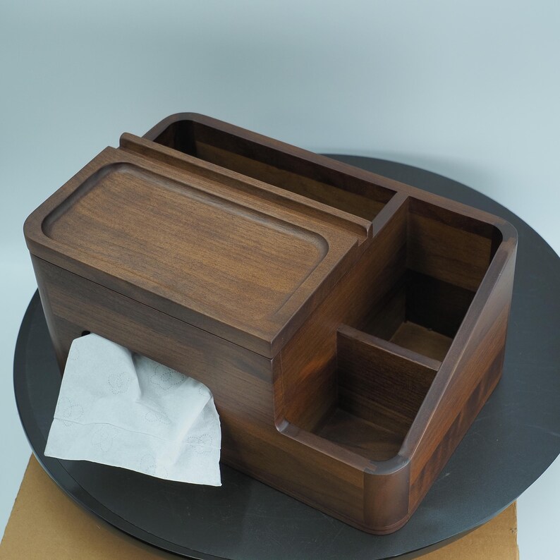 May include: A wooden desk organizer with a tissue box, pen holder, and small compartments. The organizer is made of dark brown wood and has a smooth finish. A white tissue is partially pulled out of the tissue box.
