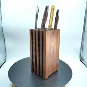 Puede incluir: Un bloque de cuchillos de madera con acabado natural contiene cuatro cuchillos. Los cuchillos tienen varios diseños de mango, incluyendo un mango plateado, de madera oscura y de bambú. El bloque es de madera maciza y tiene un diseño ranurado.