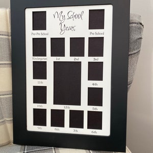 May include: Black picture frame with white matting and cutouts for photos. The frame has the text "My School Years" and labels for each grade from Pre-Pre School to 12th grade.
