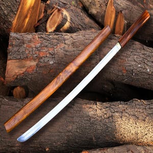 May include: A traditional Japanese katana sword with a polished steel blade and a wooden handle and scabbard. The handle and scabbard are a rich, dark brown color, and the blade is silver. The sword is resting on a pile of wooden logs.