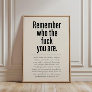 Könnte beinhalten: Ein rechteckiger Wandkunstdruck in einem hellen Holzrahmen mit schwarzem Text auf cremefarbenem Hintergrund. Der große Fettdruck lautet, Remember who the fuck you are, gefolgt von einer horizontalen Linie und einem Absatz über Selbstwertgefühl.