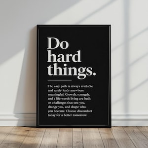 May include: A black framed wall art print featuring the white text Do hard things. followed by a horizontal line and a paragraph of text that reads: The easy path is always available and rarely leads anywhere meaningful. Growth, strength, and a life worth living are built on challenges that test you, change you, and shape who you become. Choose discomfort today for a better tomorrow.
