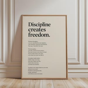 May include: A rectangular wall art print in a light wood frame featuring the black text Discipline creates freedom followed by a paragraph explaining the concept of discipline and freedom on a solid light beige background with a clean layout.