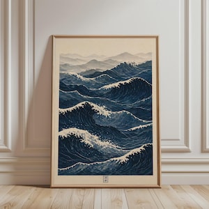 May include: Framed print of a Japanese woodblock print depicting ocean waves. The artwork features shades of blue and white, with stylized waves and a distant mountain range. The print is in a light-colored wooden frame.