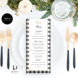 May include: A black and white checkered menu card with gold accents. The menu card features a Thanksgiving-themed menu with appetizers, main course, and dessert options. The text on the menu card reads: "Menu", "Appetizers", "Cranberry Chutney", "Roasted Butternut Squash Soup", "Baked Brie & Rosemary Crackers", "Main Course", "The Perfect Roast Turkey", "With Herbs de Provence Rub", "Spiced Cranberry Sauce", "With Orange Star Anise", "Wild Rice and Balsamic Dressing with Sausage and Sage", "Rachel Ray's Mayo Stuffing", "But Red Grapefruit", "And Cranberry Salad", "Dessert", "Light and Fluffy Carrot Souffle", "Bourbon Cranberry Bread Pudding", "Pumpkin Pie".