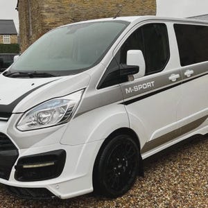 May include: White Ford Transit van with black wheels and trim. Features grey stripes and the text "M-SPORT". The registration plate reads "HG17 FPL". A modern commercial vehicle.