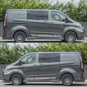 May include: Two grey custom vans are displayed, highlighting their modified features. The vans have tinted windows, custom wheels, and side panel graphics with the word "CUSTOM". The vehicles are set against a backdrop of green foliage and a stone wall.