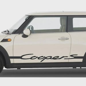 May include: Cream-colored Mini Cooper car with black accents, including the wheel arches and a side stripe with the word "Coopers" in black script. The car has silver wheels and tinted windows.
