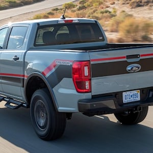 Könnte beinhalten: Ein grauer Ford Ranger Tremor Pickup-Truck fährt auf einer Straße. Er hat schwarze und rote Akzente, eine schwarze Heckstoßstange und ein Nummernschild. Das Wort "Tremor" ist auf der Seite sichtbar.