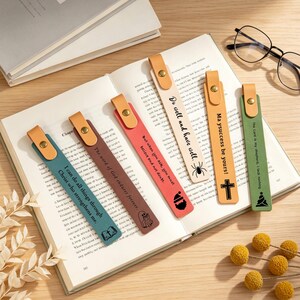 Puede incluir: Seis marcapáginas rectangulares de cuero con lengüetas de cuero color canela y remaches metálicos dorados. Cada marcapáginas presenta texto e iconos únicos: azul con una cruz, marrón con un fantasma, rojo con un gorro de Papá Noel, crema con una araña, canela con una cruz y verde con un árbol de Navidad.