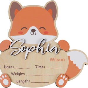 May include: Wooden fox-shaped name plaque with the name "Sophia" in cursive. The plaque has a light brown background with orange and white accents. Includes space to write birth details. The last name "Wilson" is also included.
