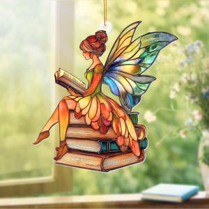 May include: A colorful fairy ornament, reading a book while sitting on a stack of books. The fairy has red hair, a green and orange dress, and multi-colored wings. The ornament hangs from a gold string.