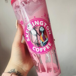 May include: A pink tumbler with a screw-on lid, filled with a pink liquid. The tumbler features a circular graphic with Jack Skellington and Sally from The Nightmare Before Christmas, with the text "SKELLINGTON COFFEE".